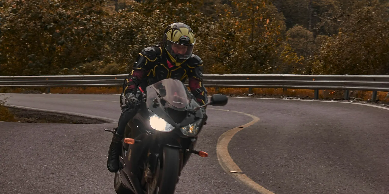 Motard sur une route sinueuse bordée d’arbres aux couleurs d’automne
